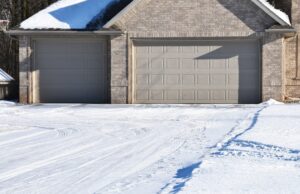Snow-covered concrete driveway leading to a two-car garage at a residential home during winter, showing tire tracks and freeze-thaw conditions common in Illinois.